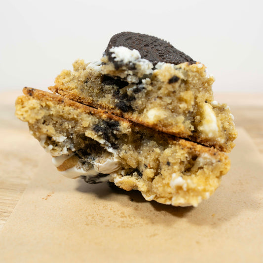 A close-up of a cookies and cream cookie with chocolate cookie crumb filling, resting on a piece of brown paper against a light background.